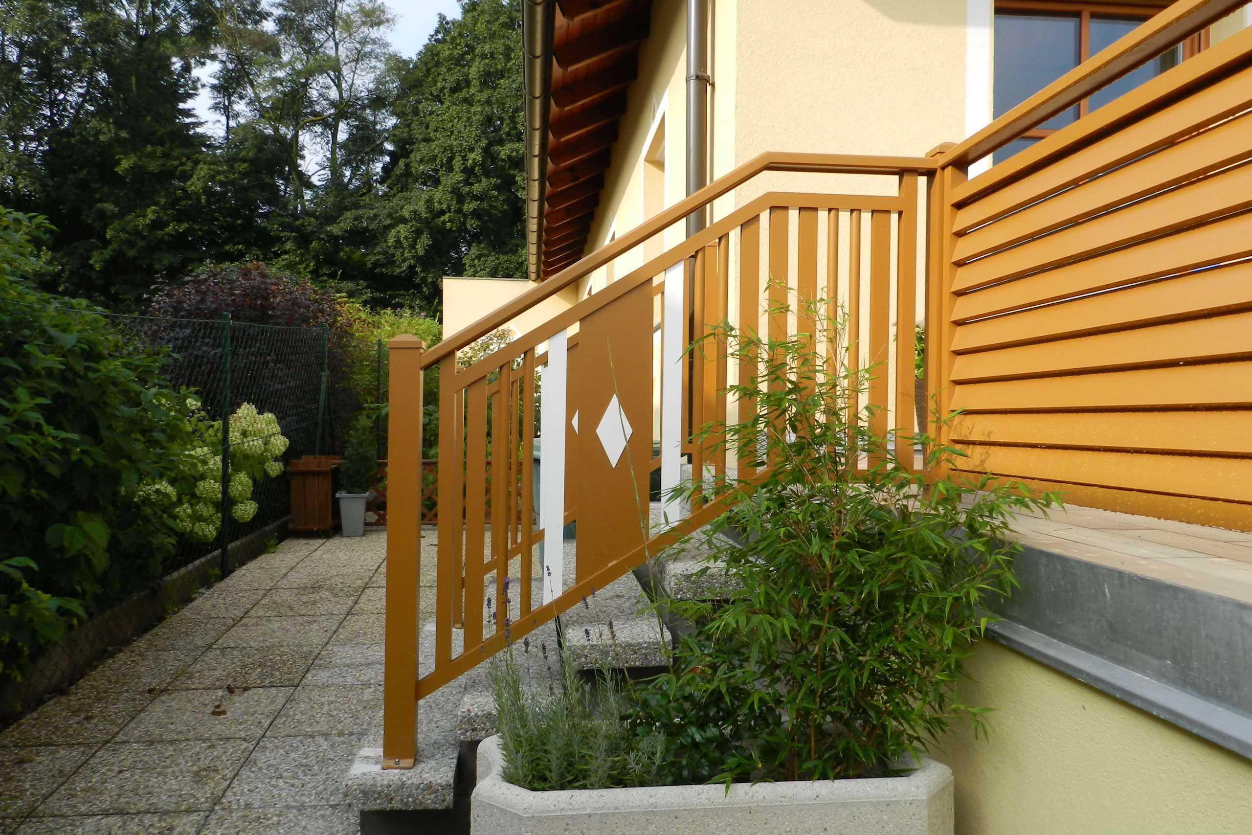 Hellbrauner Aluzaun mit weißen Elementen an einem gelben Haus