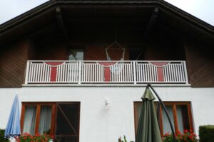 Weißer Alubalkon mit roten Elementen an einem weißen Haus mit Holzelementen an der Fassade
