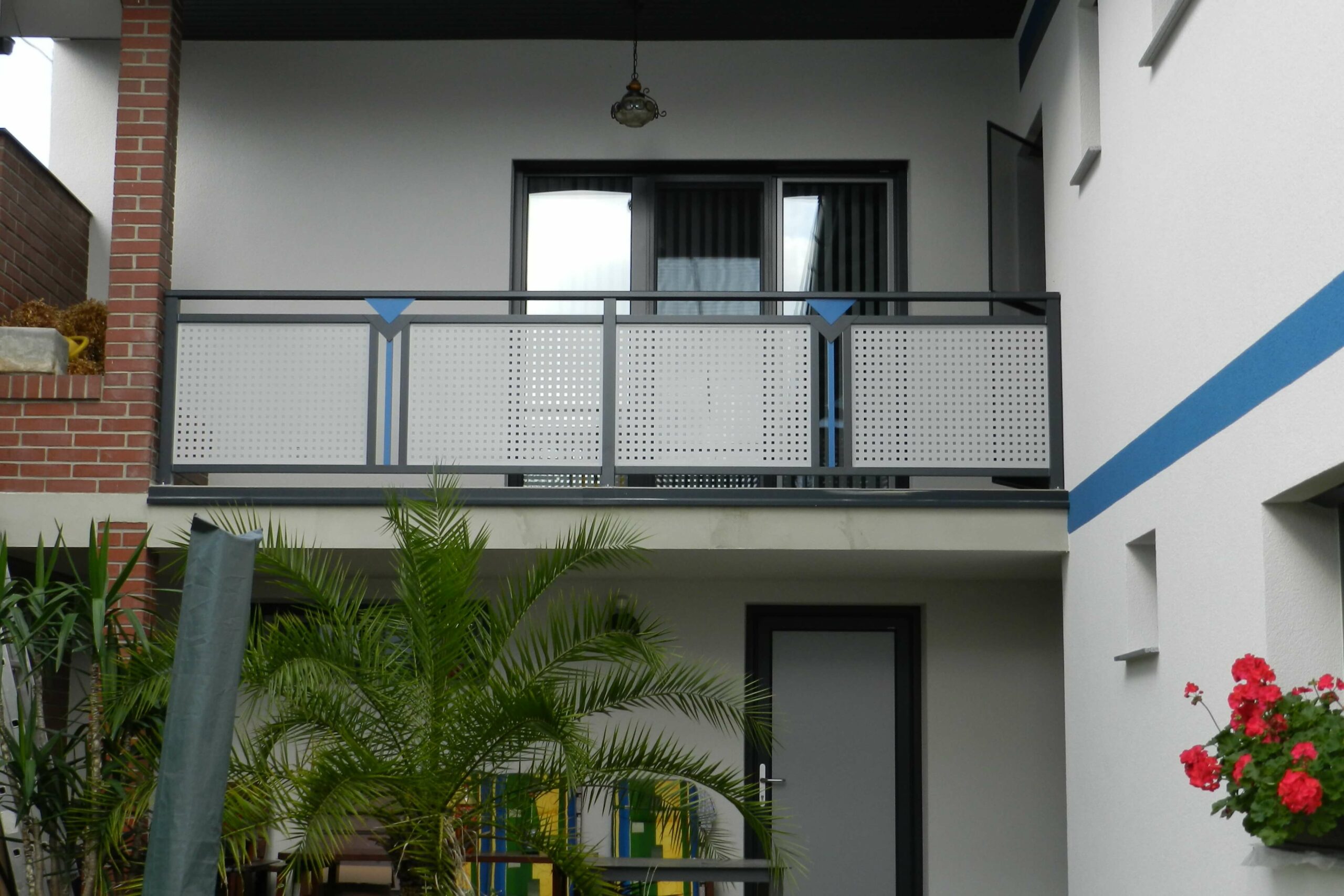 Grauer Alubalkon mit blauen Elementen an einem weißen Haus