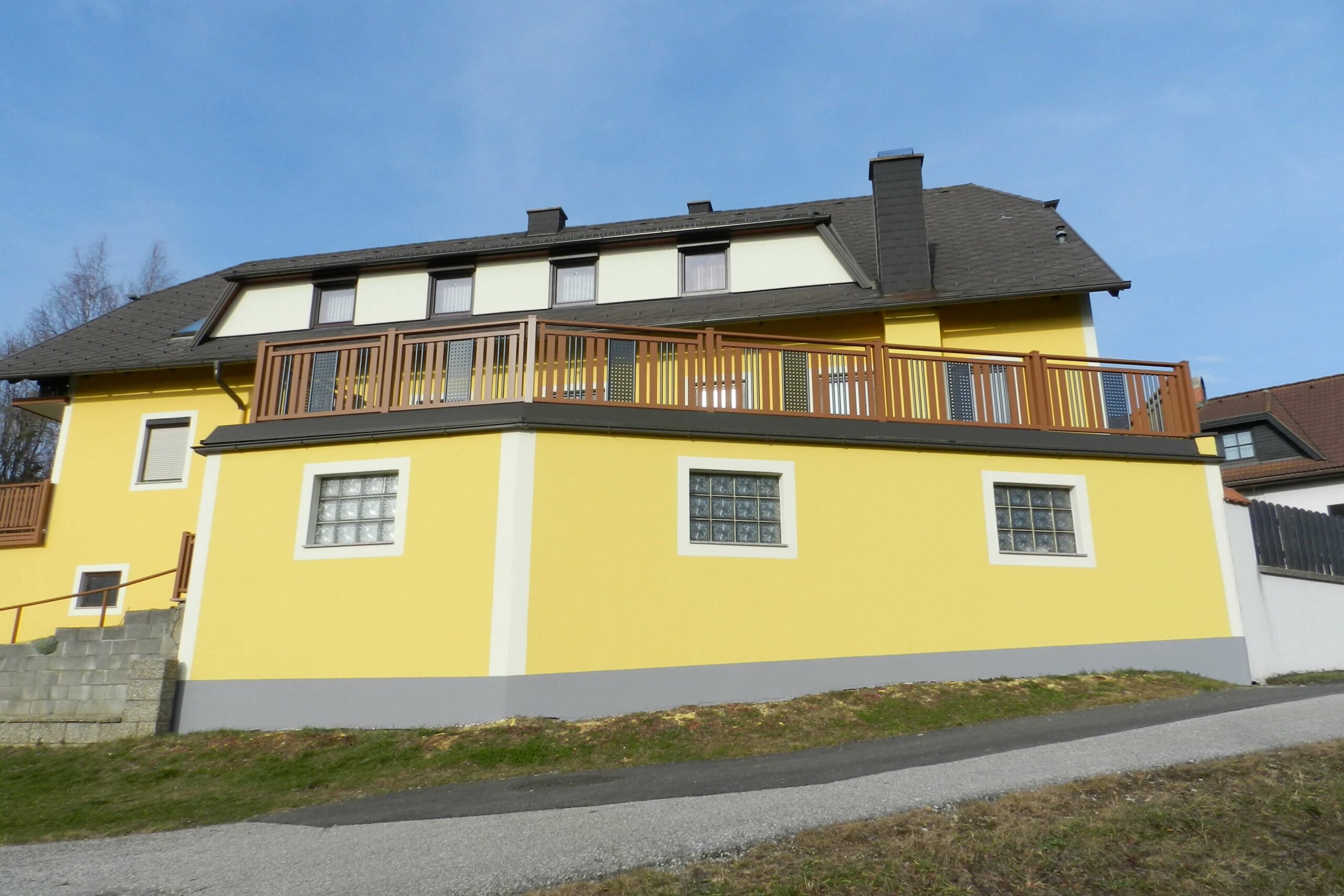 Brauner Alubalkon mit grauen Elementen an einem gelben Haus