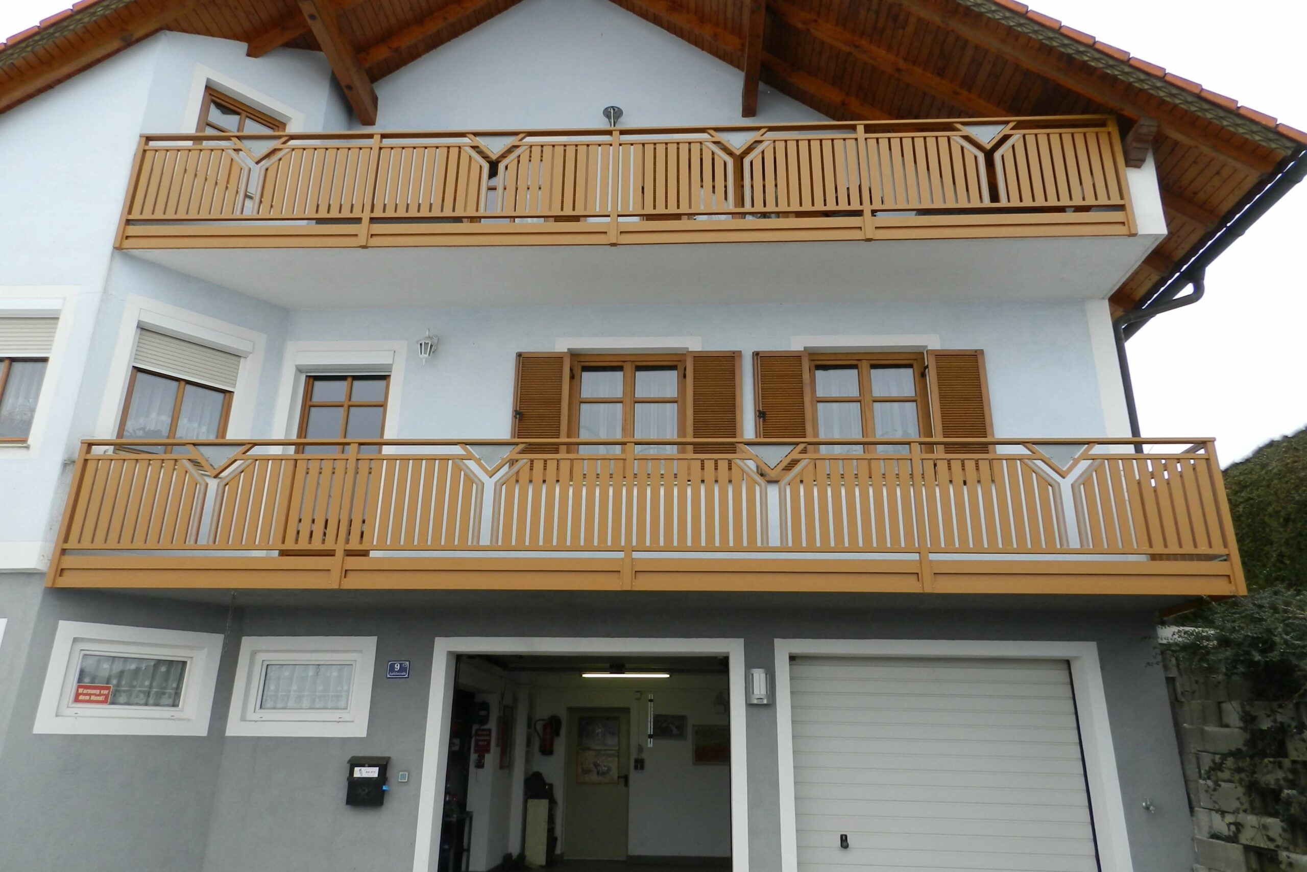 Beiger Alubalkon mit weißen Elementen an einem grauem Haus