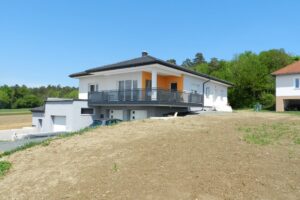 Grauer Alubalkon an einem weißen Haus mit orangenen Elementen an der Fassade