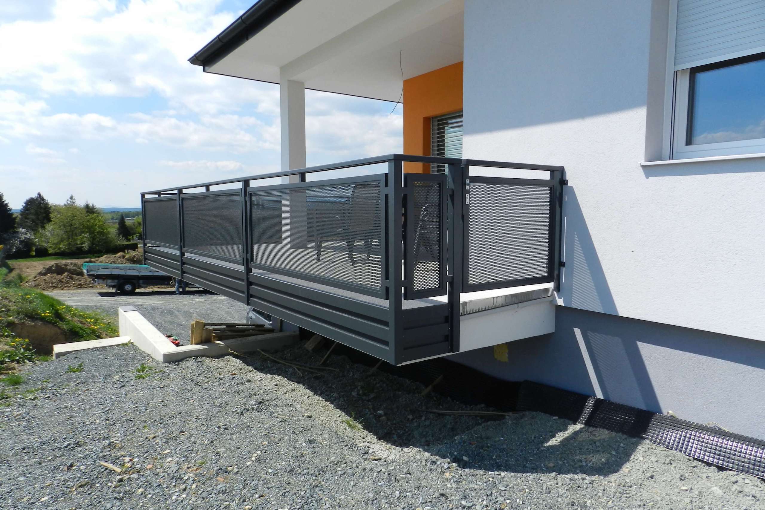 Grauer Alubalkon an einem weißen Haus mit orangenen Elementen an der Fassade