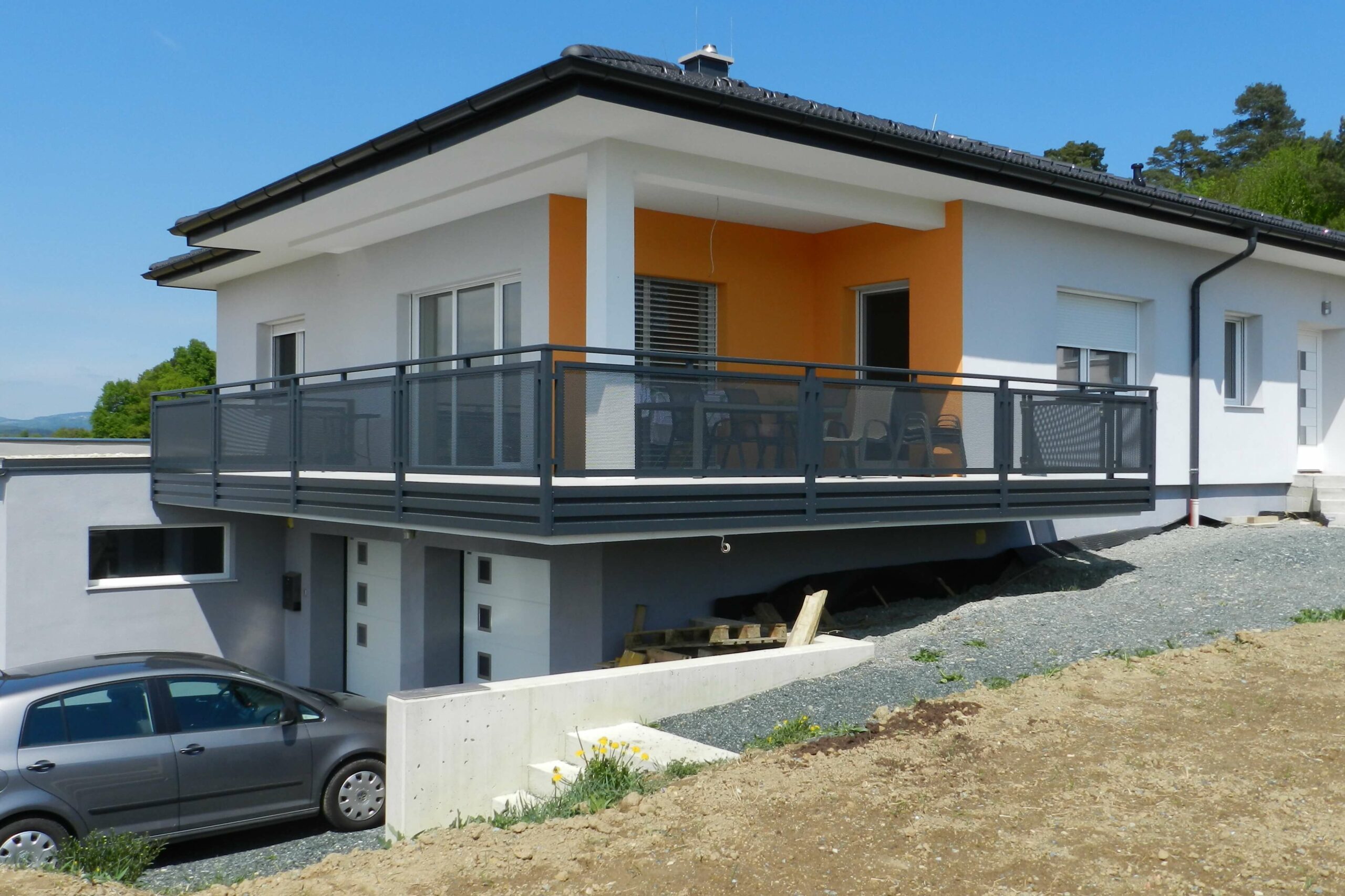 Grauer Alubalkon an einem weißen Haus mit orangenen Elementen an der Fassade