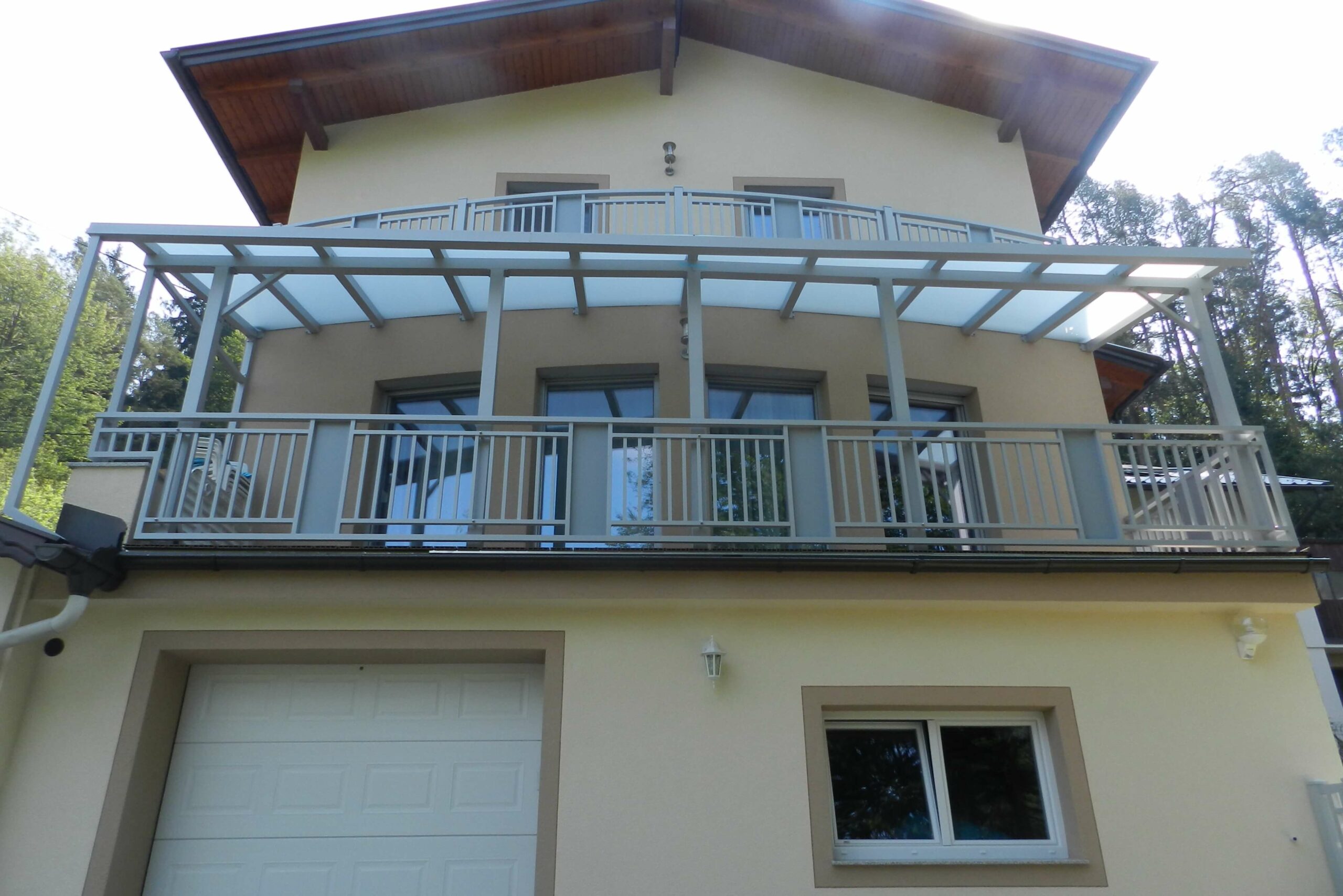 Hellgrauer Alubalkon mit Überdachung an einem gelben Haus