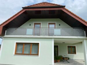 Hellgrauer Aluzaun mit Glaselemente an einem grünen Haus