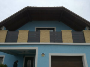 Grauer Aluzbalkon mit Steinelementen an einem hellblauen Haus