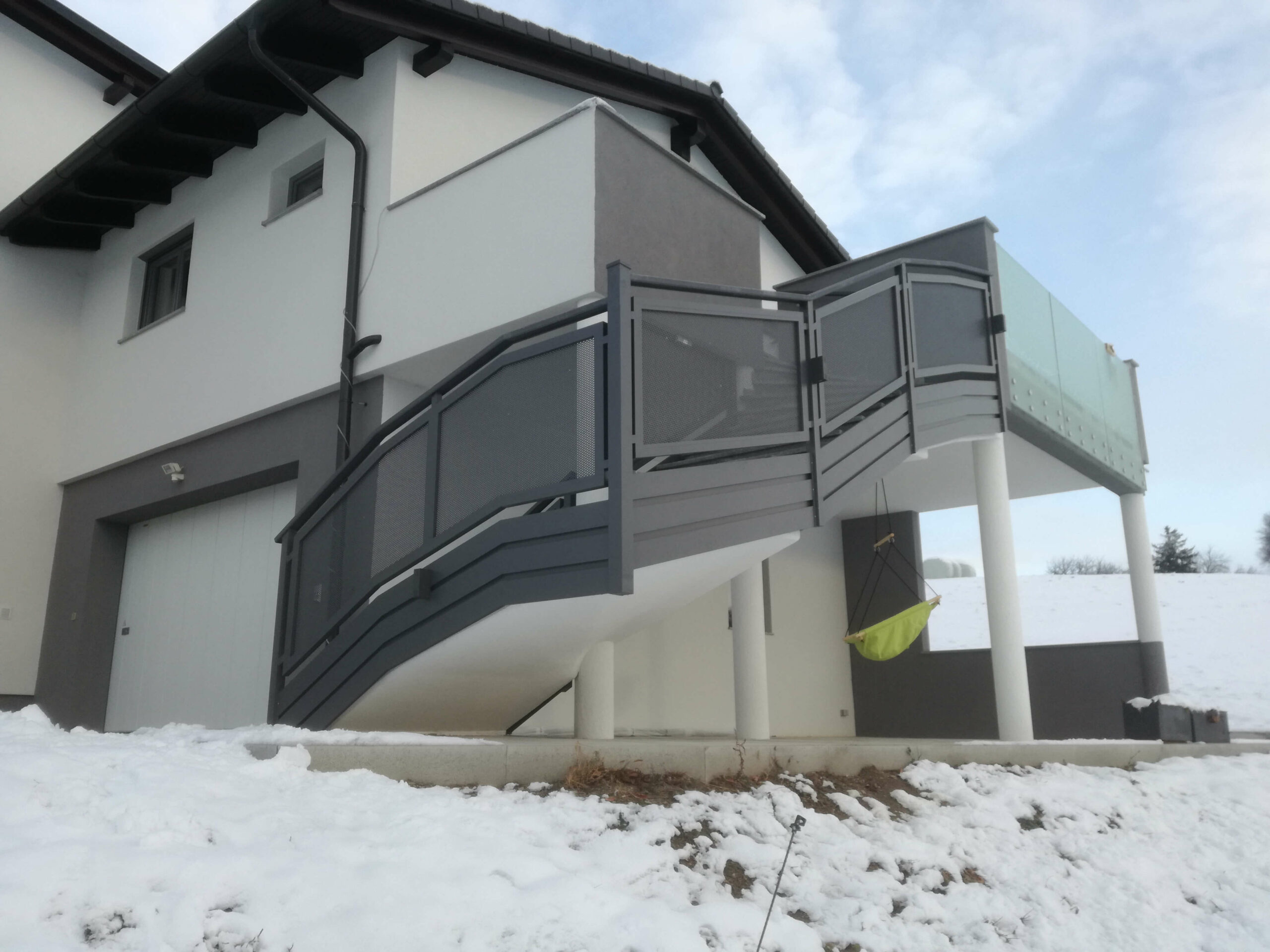 Grauer Aluzaun bei dem Stiegenaufgang eines weißen Hauses