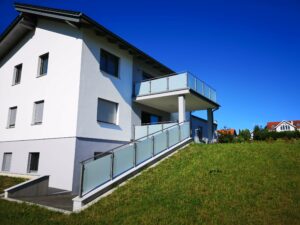 Silbener Aluzaun und -balkon mit Glaseinsätzen einem weißen Haus