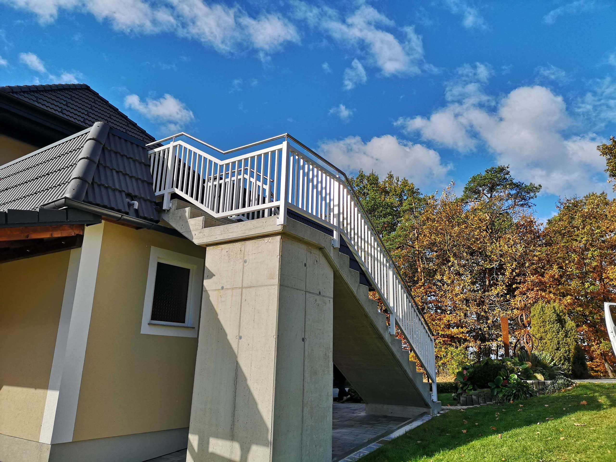 Weißer Aluzaun an einem beigen Haus mit dunkelgrauem Dach