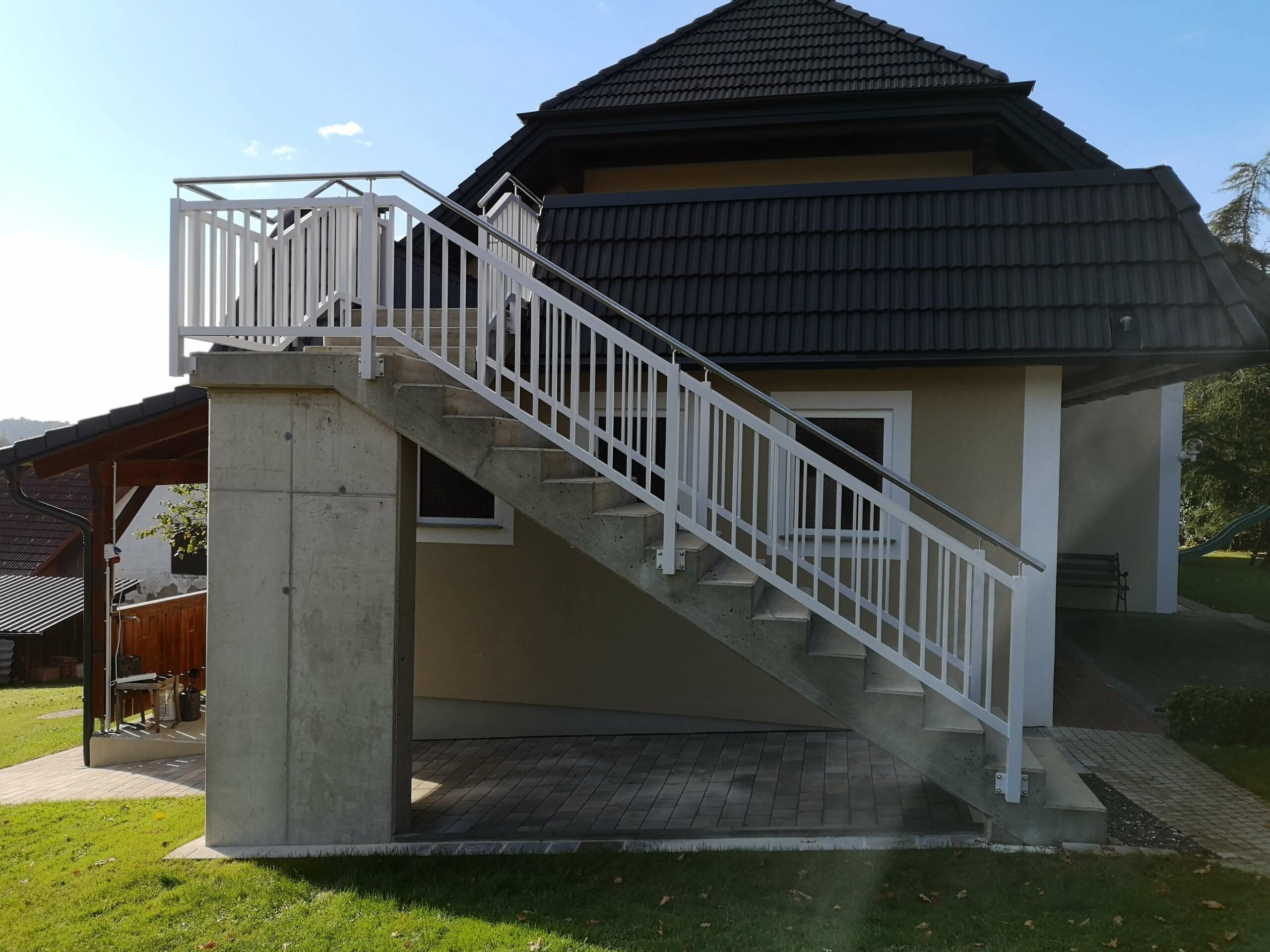 Weißer Aluzaun an einem beigen Haus mit dunkelgrauem Dach