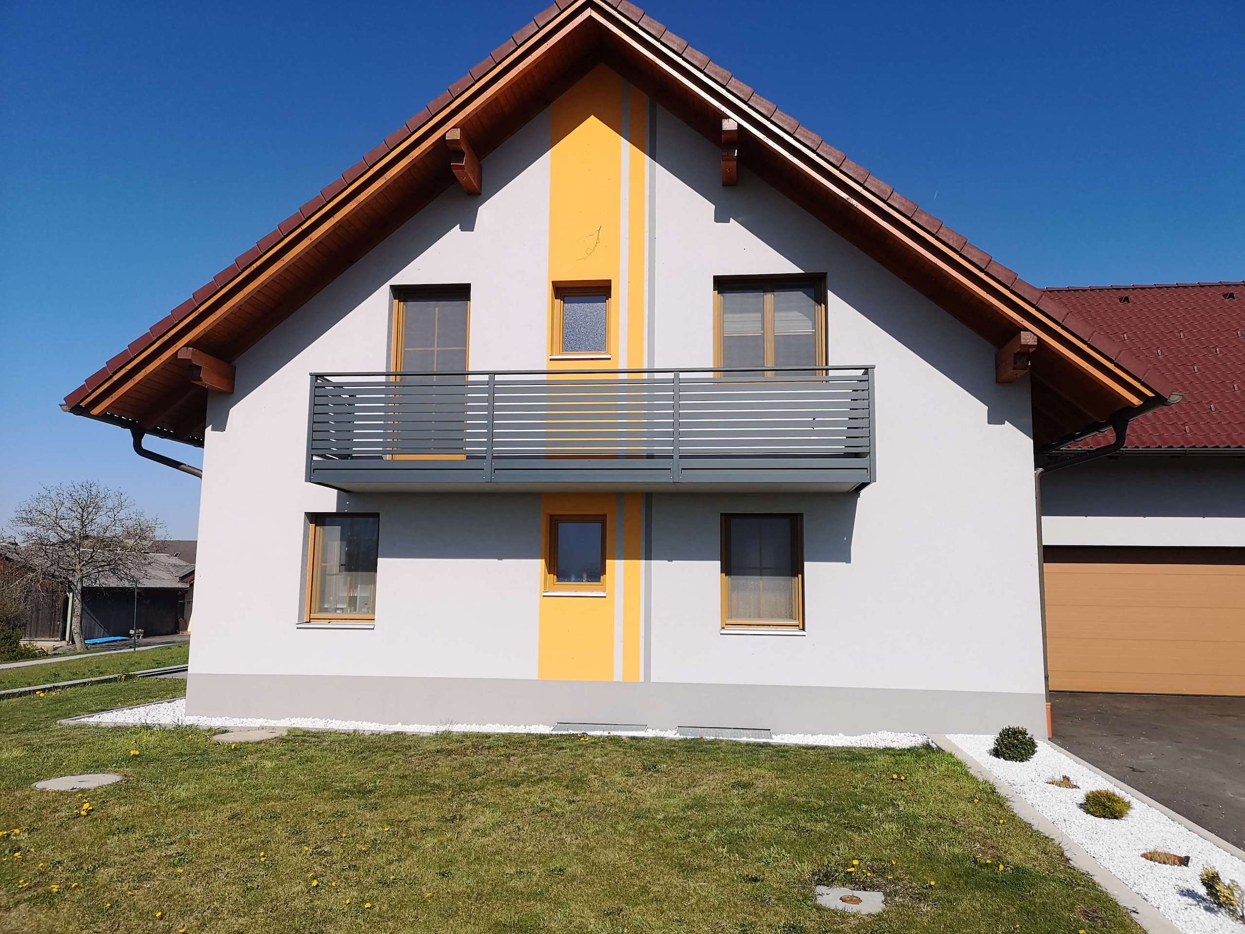 Grauer Alubalkon an einem Haus mit weißer Fassade mir orangenen Elementen