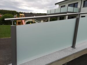 Silbener Aluzaun- und balkon mit Glaselementen an einem weißen Haus