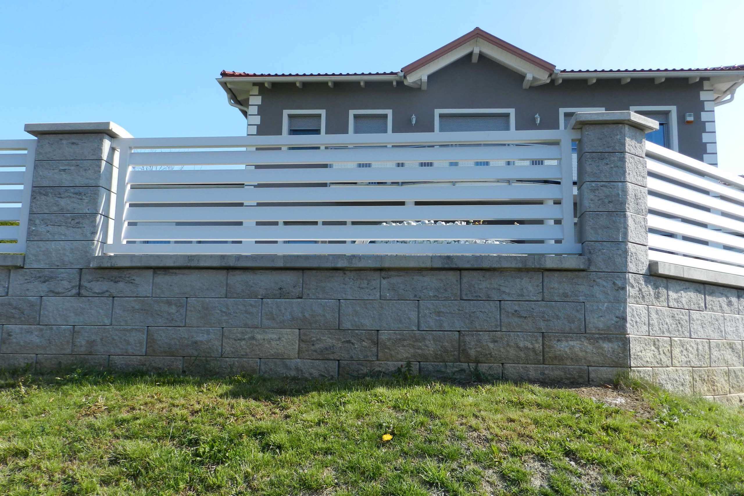 Weißer Aluzaun auf einer grauen Mauer