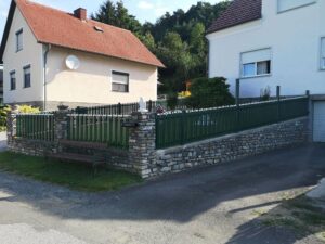 Grüner Aluzaun auf einer Mauer