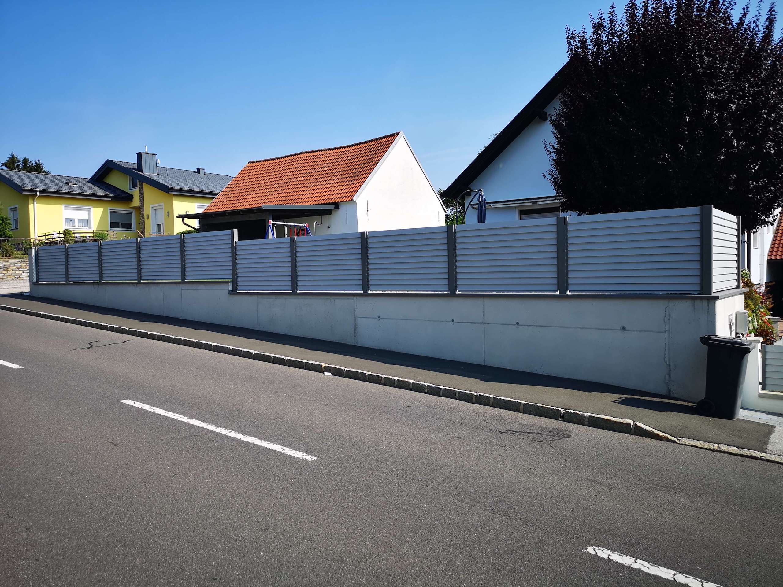 Grauer Aluzaun auf einer Mauer