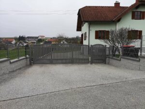 Grauer Aluzaun auf einer Mauer mit einem dunkelgrauem Einfahrtstor