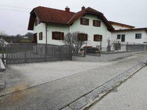 Grauer Aluzaun auf einer Mauer mit einem dunkelgrauem Einfahrtstor