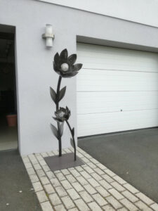 Graue Blume aus Metall vor einem Haus